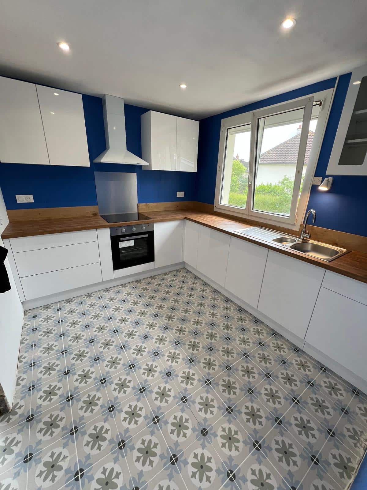 Cuisine moderne avec meubles blancs, mur bleu et sol carrelé à motifs floraux